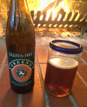 Bottle and Glass of Green's Gluten -free IPA for tasting, in front of a fireplace